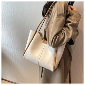 Detail shot of a beige leather tote bag with brown trim worn by a model in a trench coat