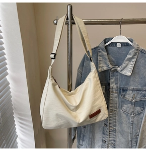 Detail of cream hobo bag showing wide shoulder strap, leather patch and zipper closure