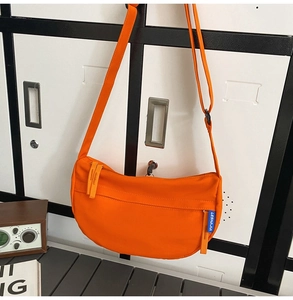 Detail view of a vibrant orange crescent crossbody bag featuring a blue side label and zipper