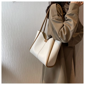 Detail of a large cream leather tote bag with brown trim worn by a model in a trench coat