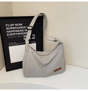 Detail of light gray nylon crossbody tote bag showing logo patch and adjustable strap