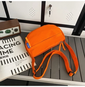 Detail of orange nylon crossbody bag with double zippers and adjustable strap on a grey surface