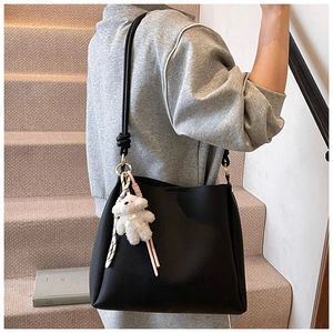 Détail du sac seau en cuir grainé noir avec bandoulière nouée et breloque ours peluche