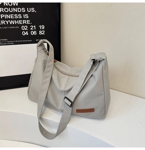 Detail of light grey nylon tote bag showing brown leather logo tag and fabric texture