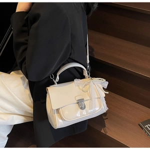 Detail of a creamy white leather square bag with a lace bow and pearl charm ornament