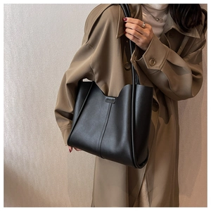 Minimalist black leather tote bag with vertical stitching shown on model in trench coat