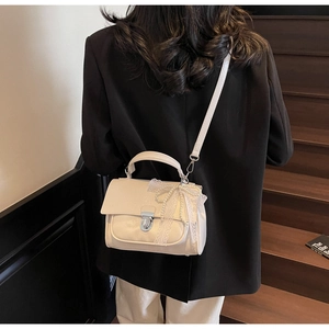Detail of cream square bag with pearl chain and lace bow on a black blazer