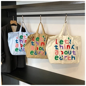 Detalle de bolsos de lona con eslogan bordado colorido Let's think about earth