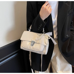 Detail of cream square crossbody bag with lace bow, pearls, and silver turn-lock