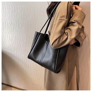 Close-up of a large black matte leather tote bag worn with a stylish khaki trench coat