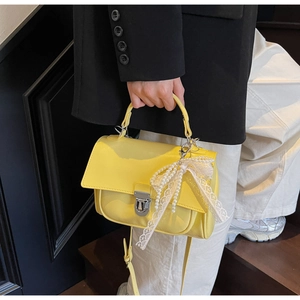 Detail of yellow crossbody bag with white lace bow and pearls held by a model