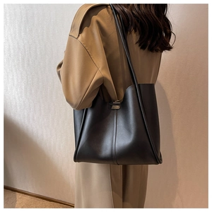 Detail of a black leather tote bag with vertical stitching shown on model's shoulder