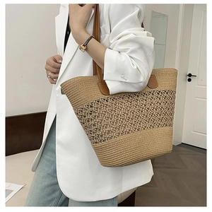 Detail of hand-woven straw tote bag with leather straps on a model in white blazer