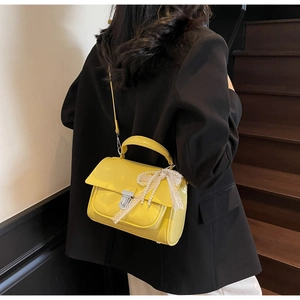 Detail of yellow shoulder bag featuring pearl lace bow and silver metallic twist lock
