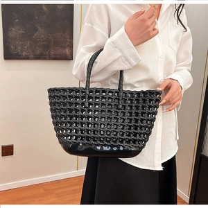 Close-up of black hollow-out woven tote bag with round handles and solid glossy base