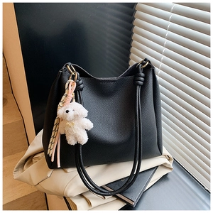 Détail du sac seau en cuir noir avec breloque ours en peluche et ruban rayé décoratif