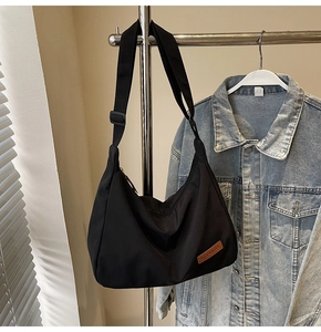 Detail of black nylon crescent bag featuring a brown leather brand tag and adjustable strap