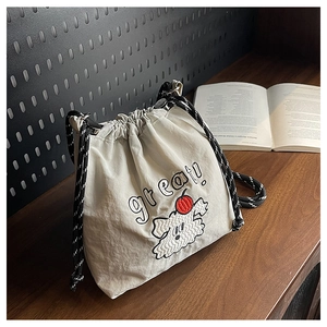 Detail der cremefarbenen Nylon-Beuteltasche mit Hunde-Stickerei und gewebtem Schultergurt