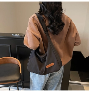 Model wearing a large black canvas crossbody hobo bag with adjustable wide strap and logo