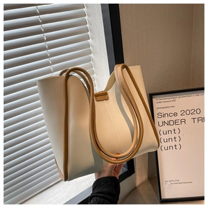 Detail of a large cream tote bag featuring brown shoulder straps and a modern bucket design