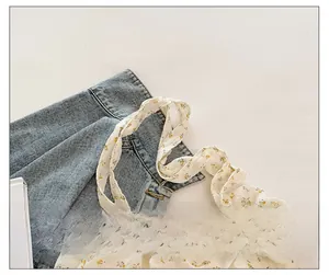 Détail de la bandoulière en toile fleurie blanche sur fond de denim bleu clair