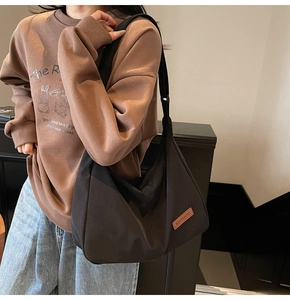 Detail of the minimalist black tote bag with a brown leather logo patch on the side