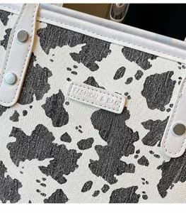 Detail van de draagtas met koeprint, leren label en metalen studs op canvas materiaal