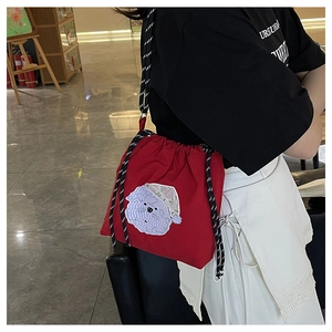 Detail der roten Nylon-Beuteltasche mit lila Stickerei und gewebtem Trageriemen am Modell
