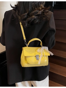 Vibrant yellow gloss handbag with pearl bow charm worn over a classic black blazer