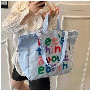 Detalle de un bolso tote azul con letras coloridas 'let's think about earth' bordadas