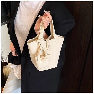 Detail of off-white lychee pattern leather bucket bag with mini pendant charm accessory