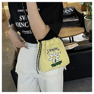 Detail der gelben Nylon-Umhängetasche mit Gänseblümchen-Stickerei und gepunktetem Gurt
