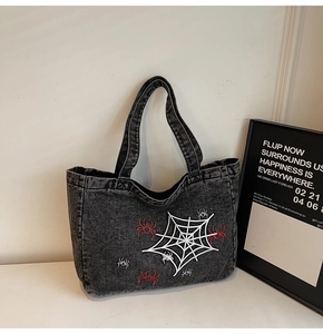 Detail of dark grey washed denim tote featuring white spider web embroidery and spiders