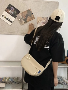 Minimalist beige half-moon crossbody bag in nylon shown in a casual lifestyle setting