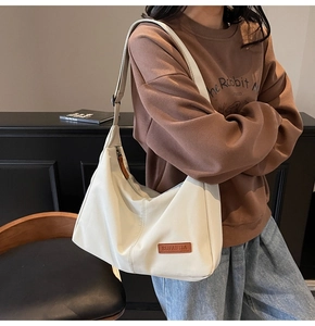 Detail shot of cream-white tote bag with brown leather logo patch and adjustable strap