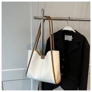 Detail of contrast stitch tote bag with brown straps hanging against a gray wall background