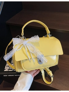 Yellow PU leather square handbag with lace bow and pearl charm on a wooden background