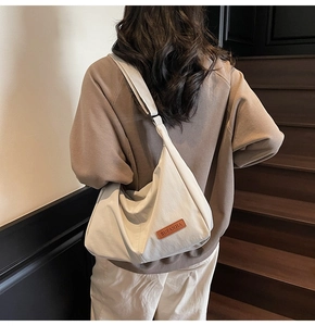 Detail of minimalist cream canvas crossbody bag with brown leather tag and wide strap