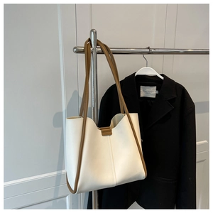 Detail of minimalist cream tote bag with brown trim hanging next to a black blazer