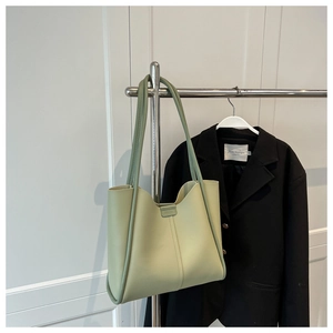 Detail of light green leather tote bag with long straps hung next to a black blazer