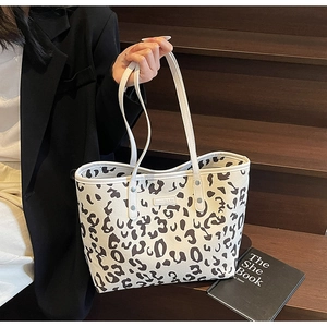 Detailopname van de tote bag met koeprint, metalen label en witte handvatten