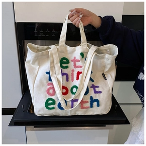 Detalle del bolso tote de lona blanco crudo con letras bordadas coloridas y relieve suave