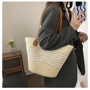 Detail of hollow woven straw tote bag with brown leather shoulder straps in a home setting
