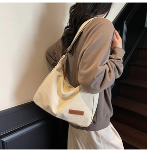 Close-up of the beige canvas tote bag side detail with a brown leather brand logo patch