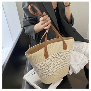 Detail of hollow woven pattern on straw tote bag with brown leather handle accents