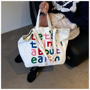 Detalle del bordado de chenilla de colores con eslogan en el bolso tote de lona blanca