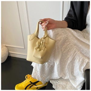 Detailed view of cream bucket bag with lychee texture held by a model in a lace dress
