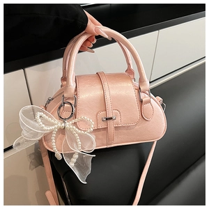 Detail of pink glossy handbag with a large white mesh bow and pearl accents on the side