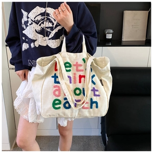 Detalle del bordado de arcoíris colorido en bolso tote de lona blanca usado por modelo