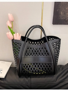 Black hollowed-out jelly tote bag with woven design and pink tulips on a leather surface